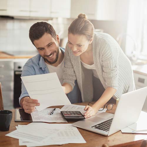 A happy couple is looking at a paper while smiling behind of a table