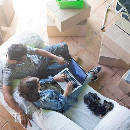 A couple looking at laptop in a living room of new house on moving day